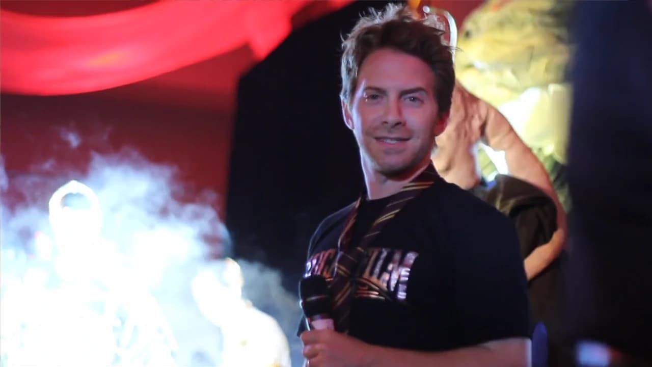 Seth Green stands in saturated red stage light and theatrical haze at Star Wars Celebration VI.